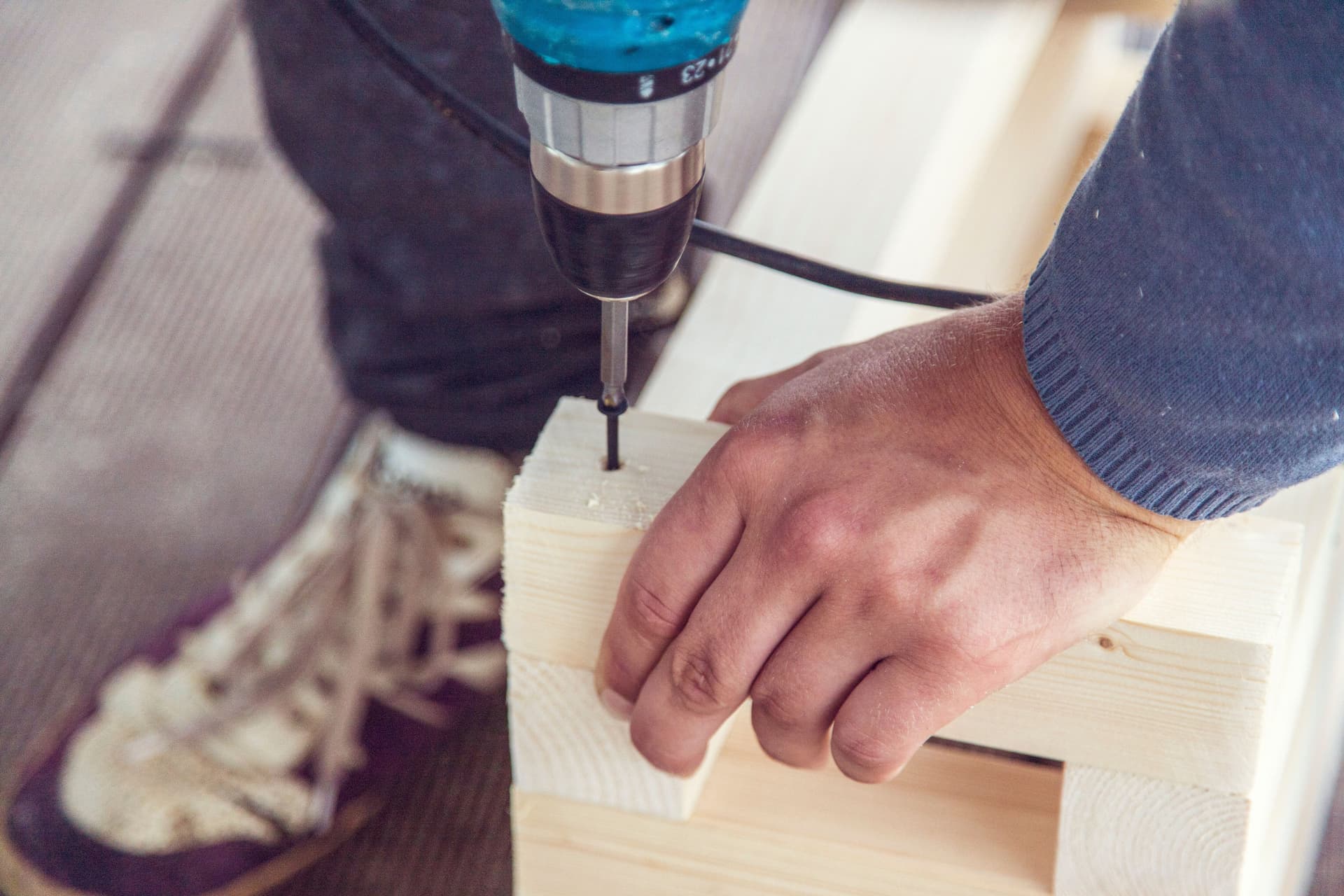 Hands drilling into a wooden board in a workshop.