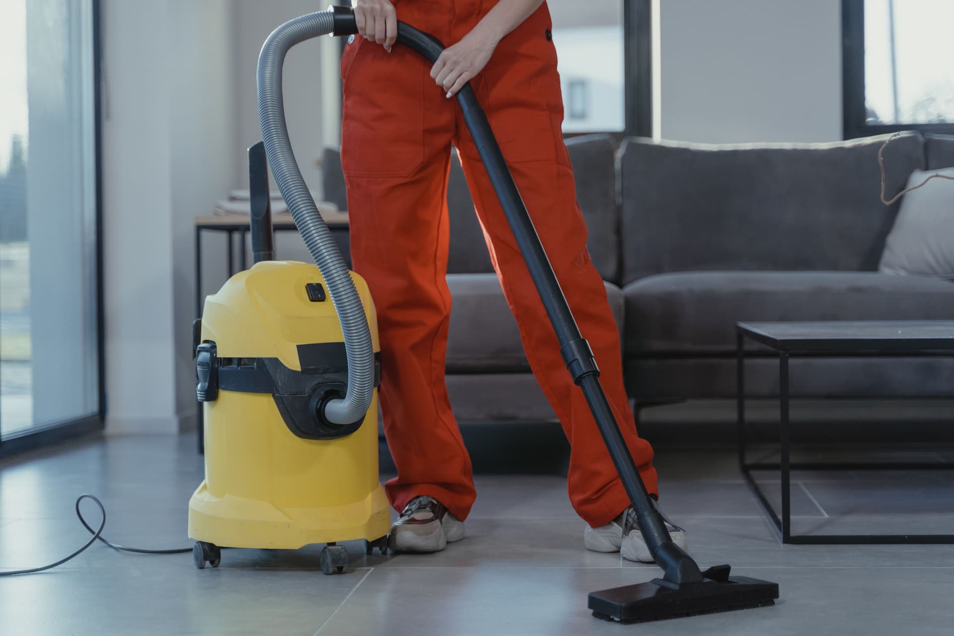 Person in red coveralls vacuuming a living room.