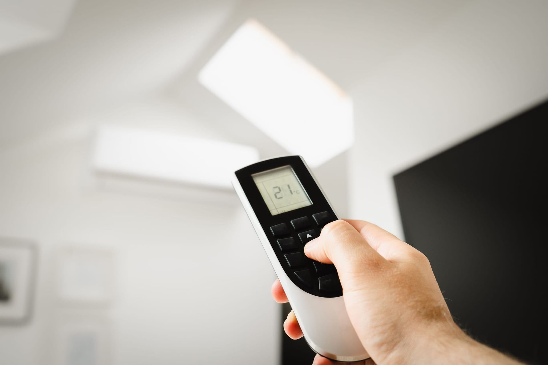A hand pointing a remote set to 21 at a wall-mounted air conditioner.