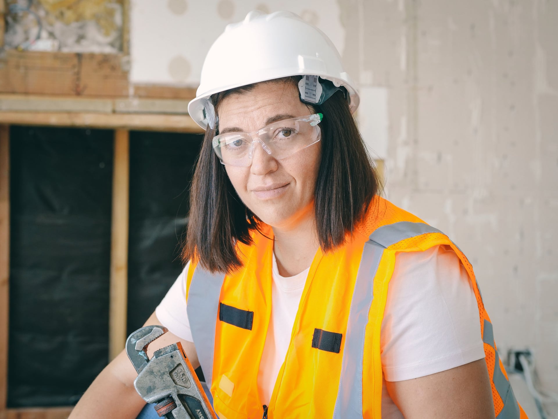 Person in safety gear holding a wrench indoors.