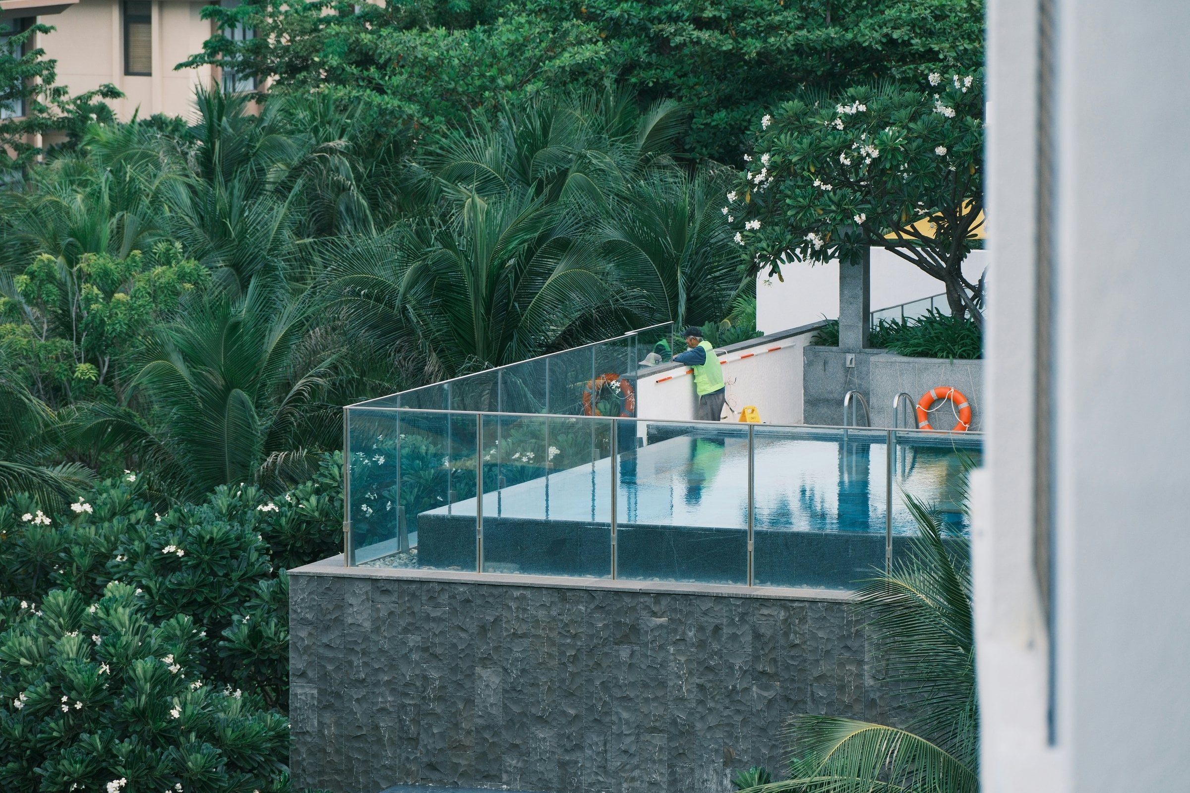 A person cleaning a swimming pool surrounded by greenery.