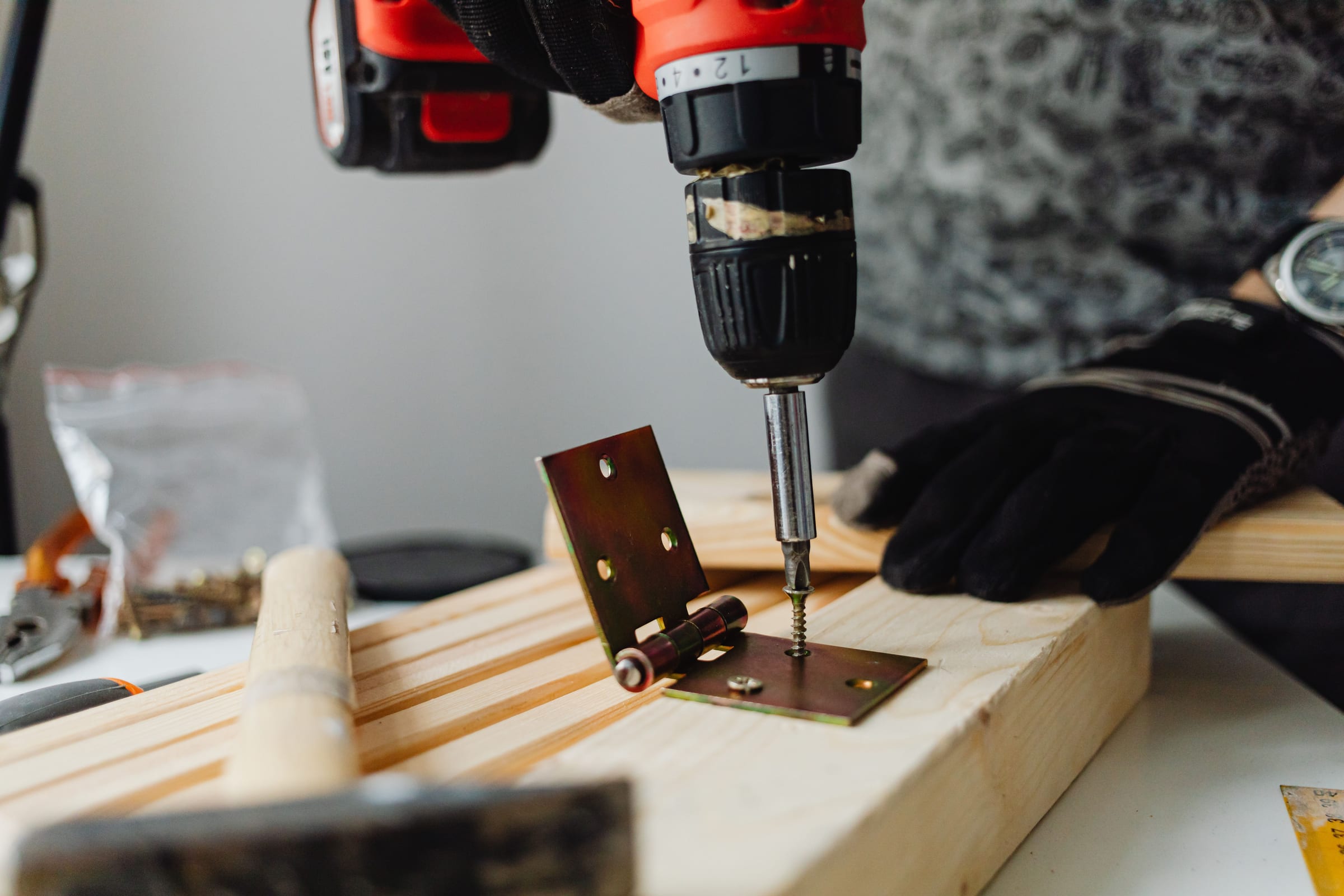 A carpenter drills a brass hinge into a pine board on a workbench.