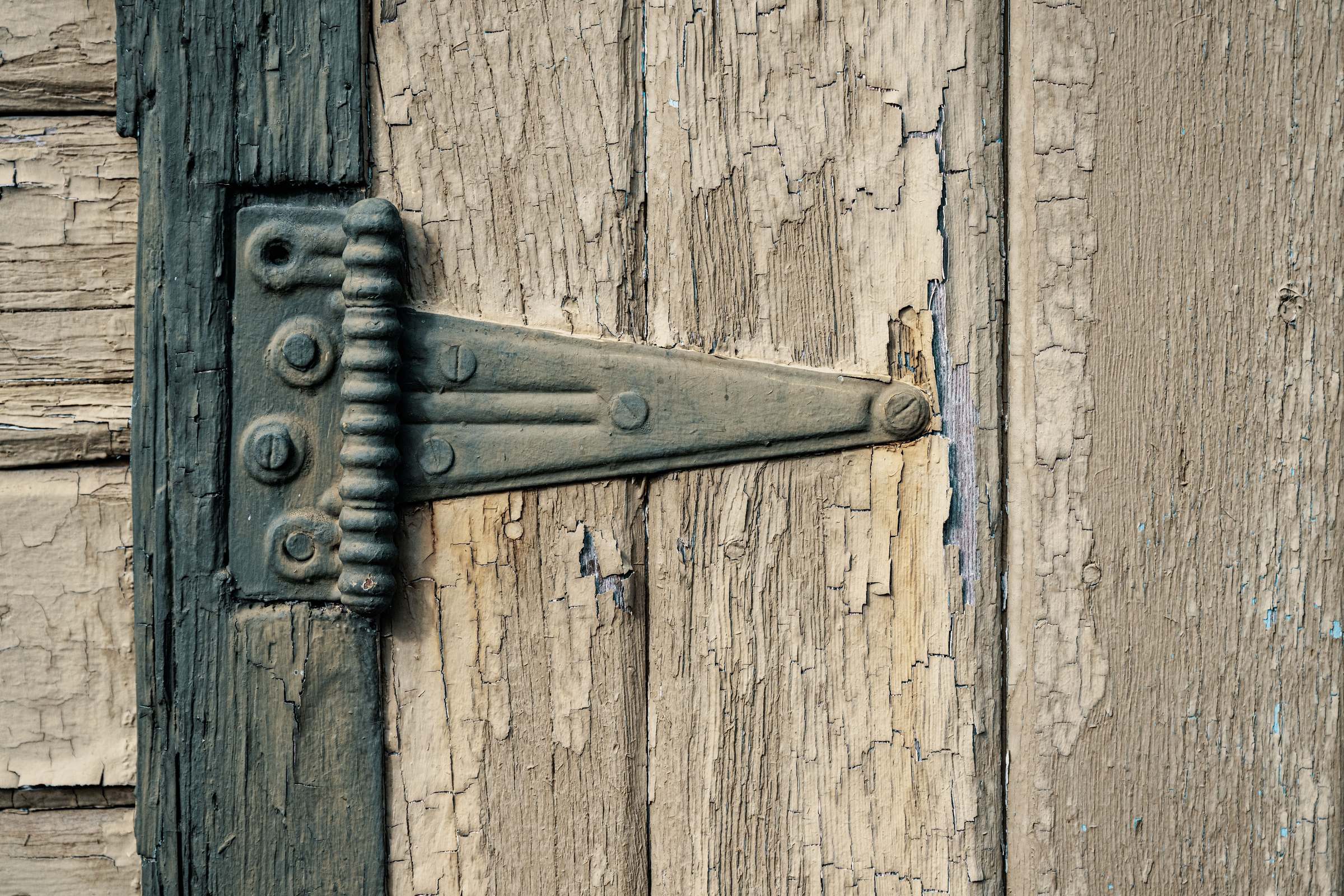 A metal strap hinge on a weathered wooden door with peeling paint.