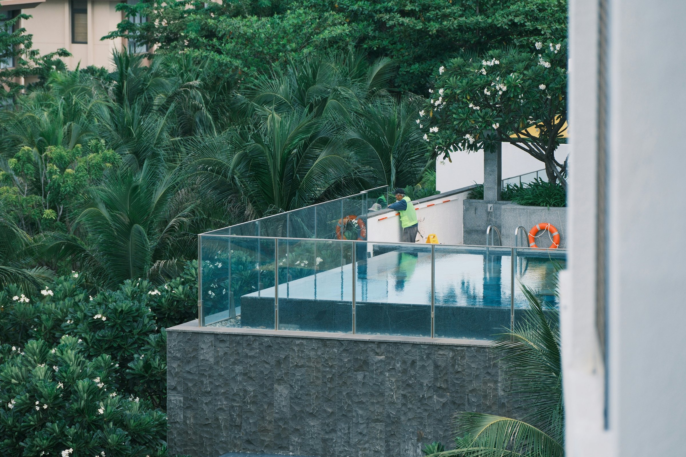 A person cleaning a swimming pool surrounded by greenery.