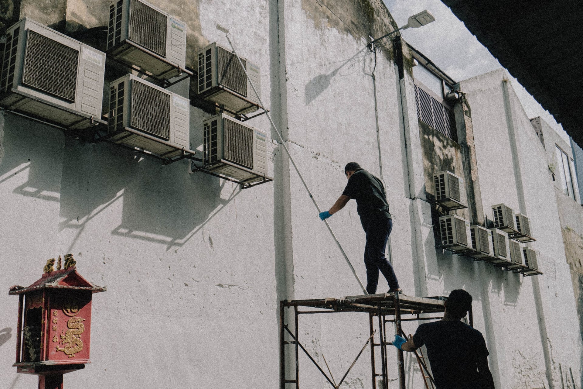 Two people on a scaffold servicing air conditioning units on a building.