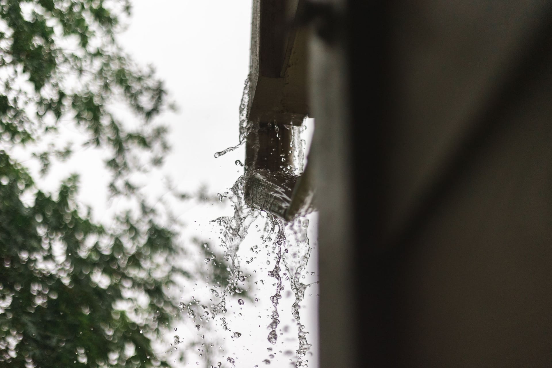 Rainwater pouring from the end of a gutter during a downpour.