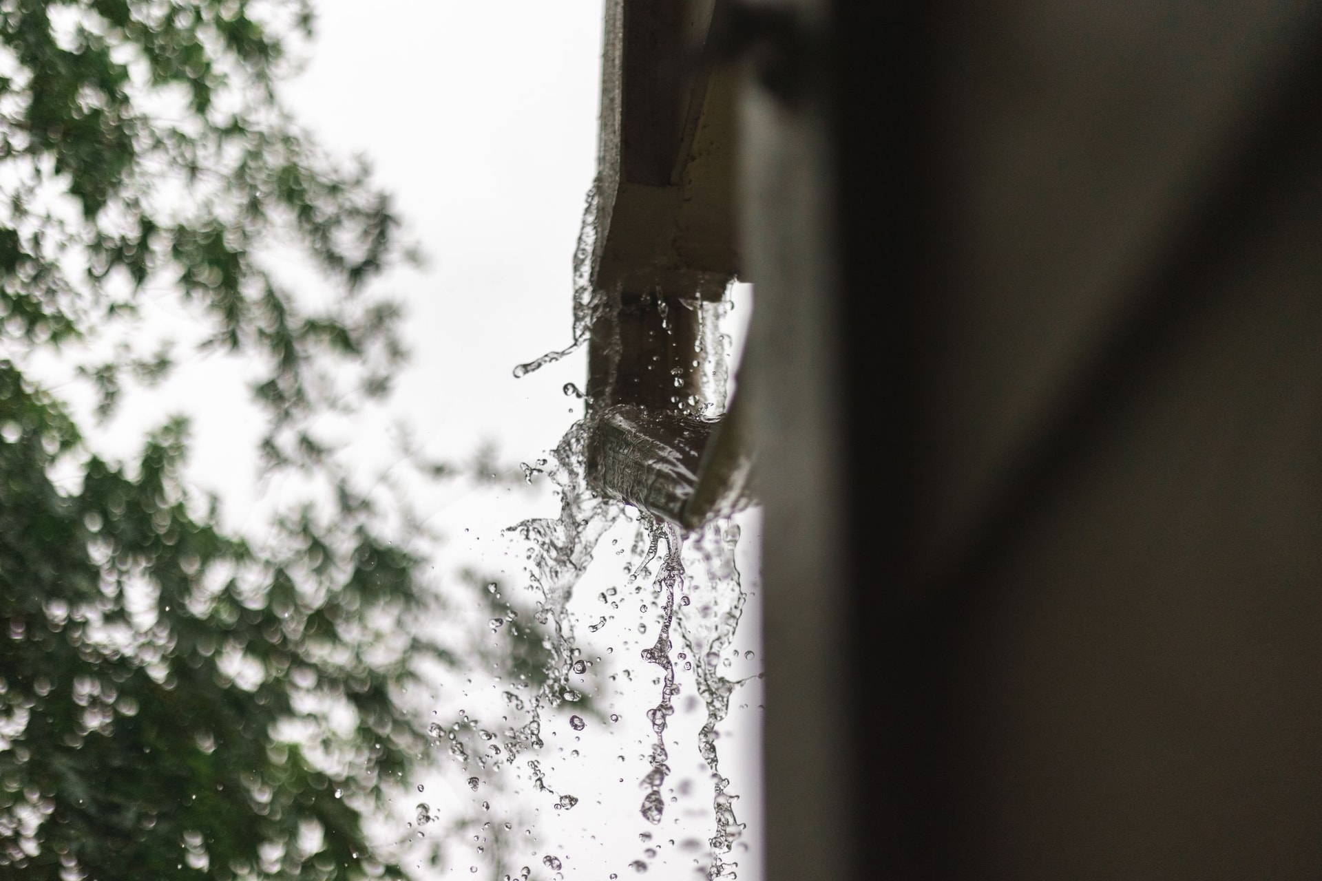 Rainwater pouring from the end of a gutter during a downpour.