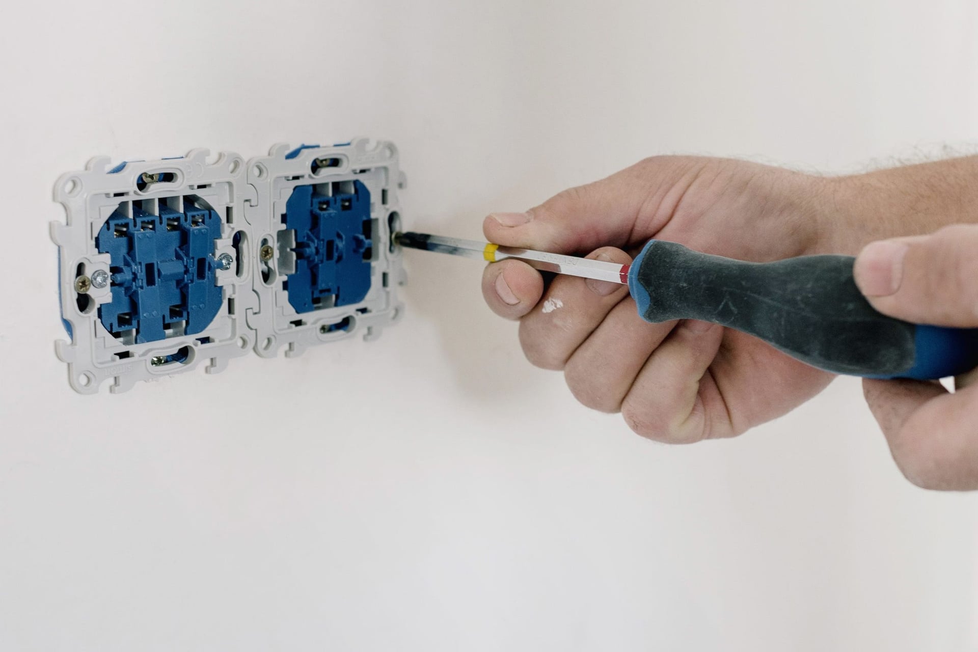 Hands fitting a wall socket with a screwdriver.