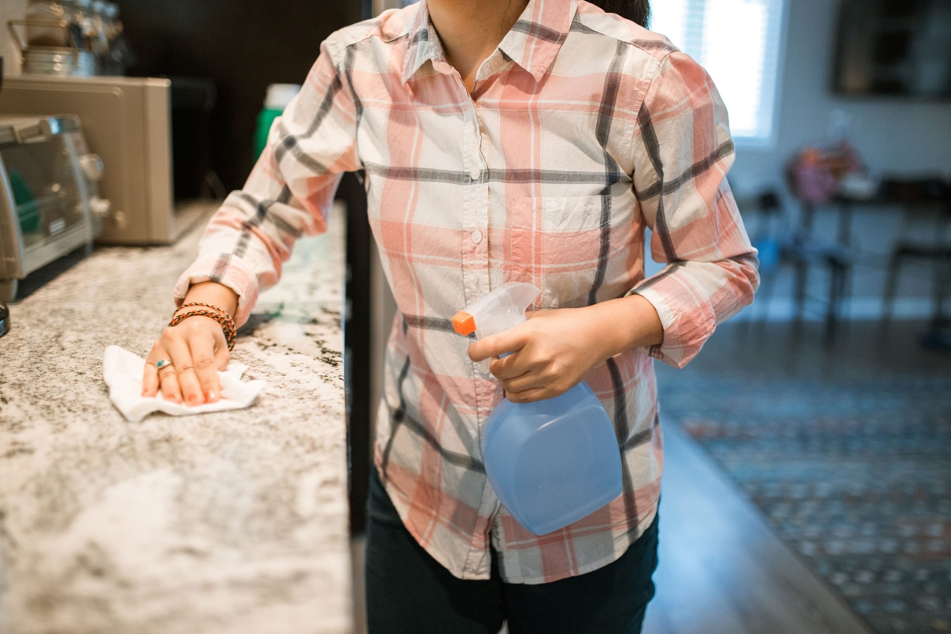 Person wiping a kitchen counter with a spray bottle and cloth.
